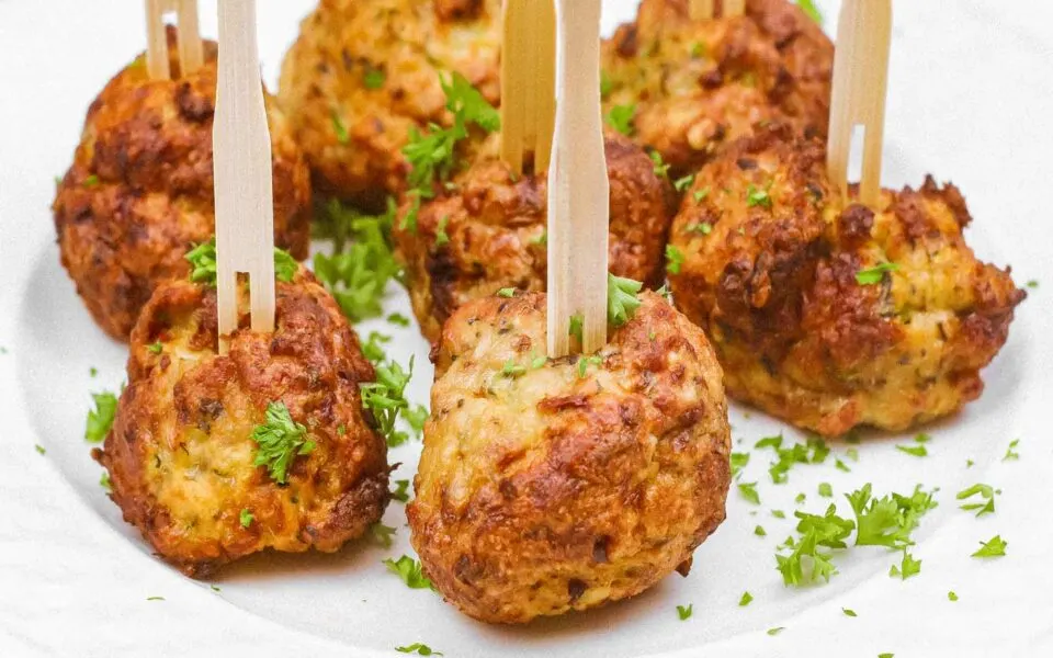 A white plate with several air-fried chicken meatballs garnished with parsley and wooden picks.