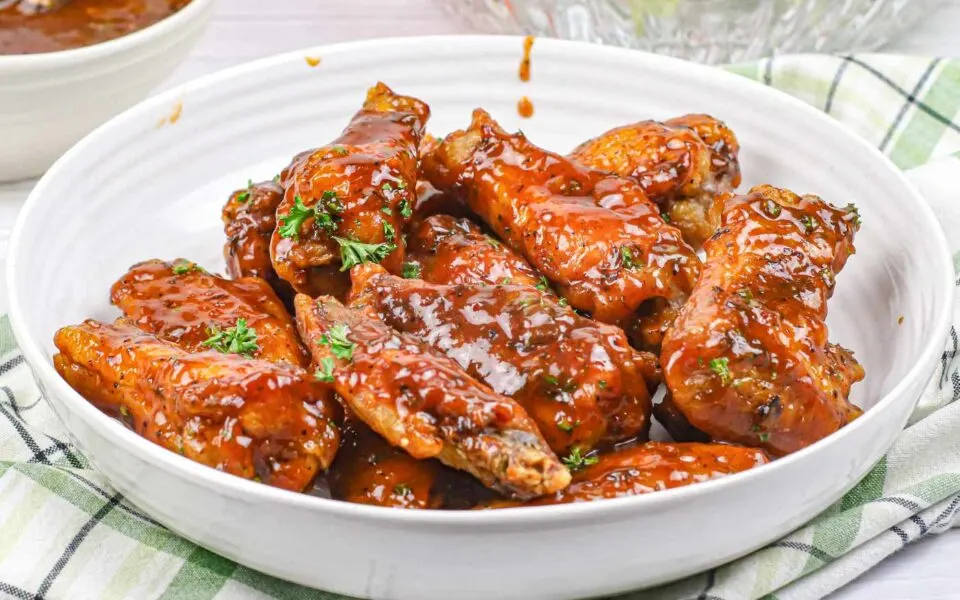 Crispy jerk chicken wings with a spicy glaze, served on a white plate with garnish.
