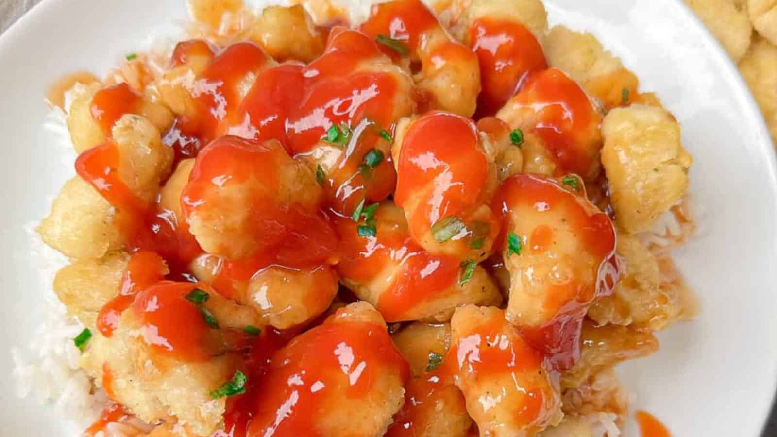 A plate of sweet and sour chicken in red sauce, topped with chopped herbs, served over white rice.