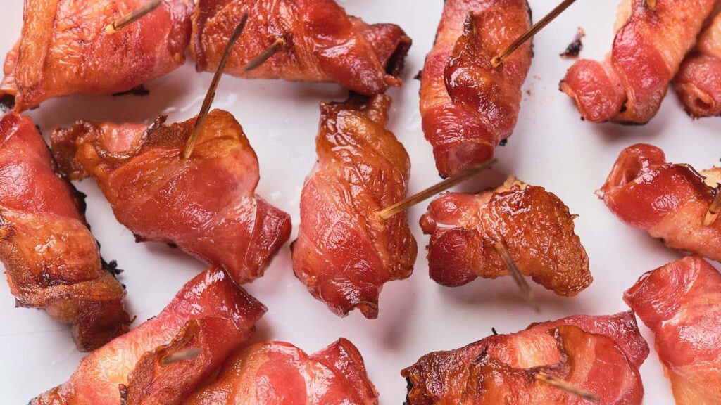 Cooked bacon-wrapped pieces secured with toothpicks are arranged on a white surface.