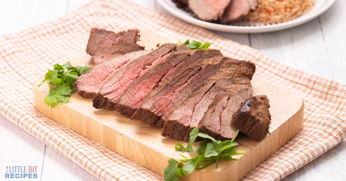 Slices of baked carne asada on small wood cutting board.
