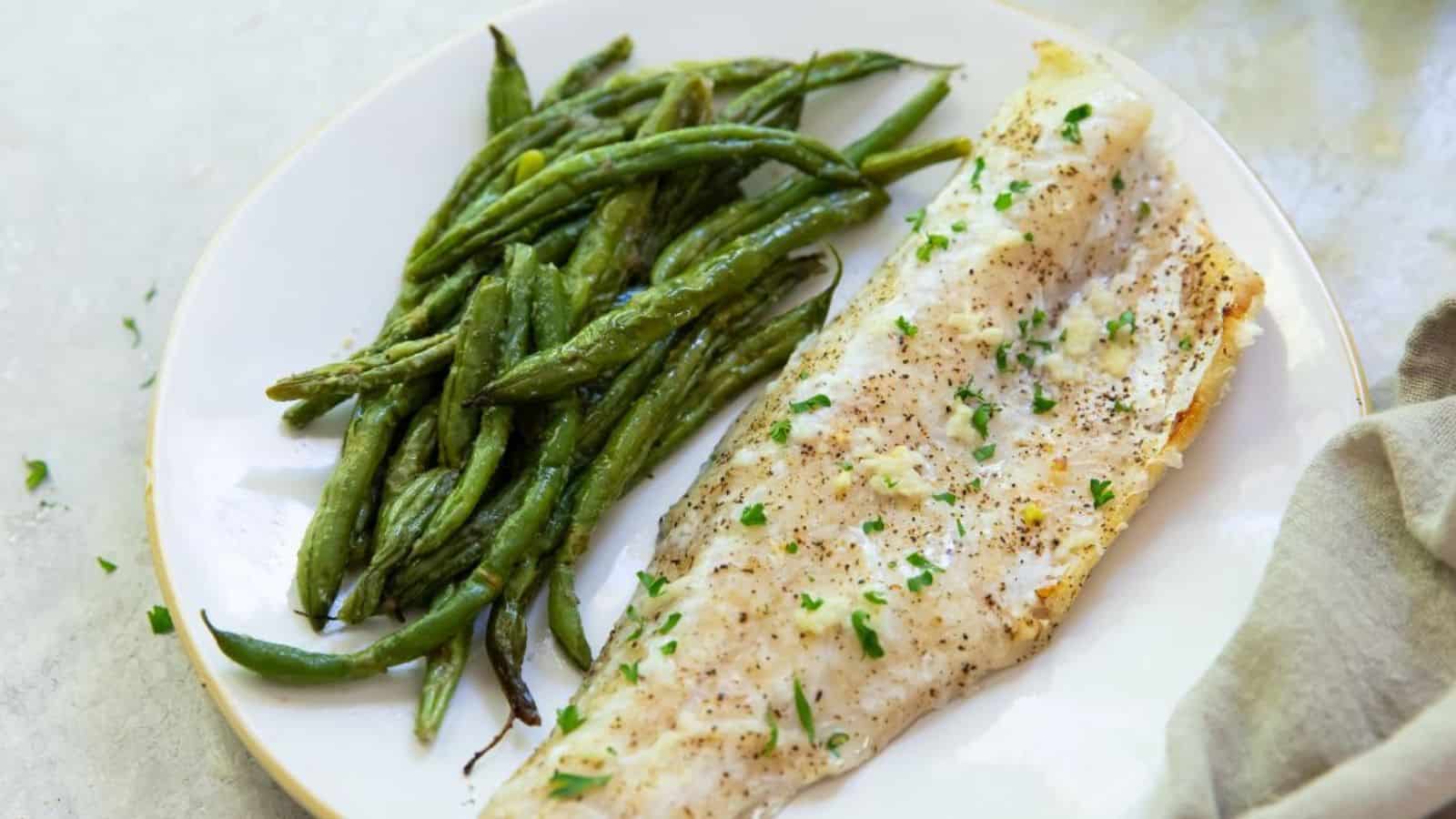 Broiled Walleye on a white plate with green beans, parsley, garlic, salt, pepper, and a fork