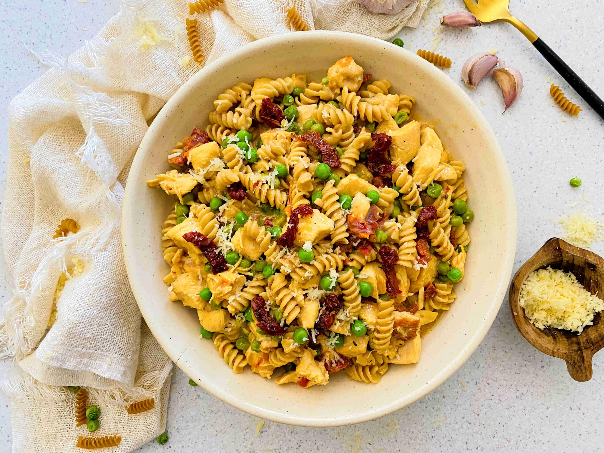 white bowl with chicken pasta with sundried tomatoes and peas and garlic and a light linen around the bowl.