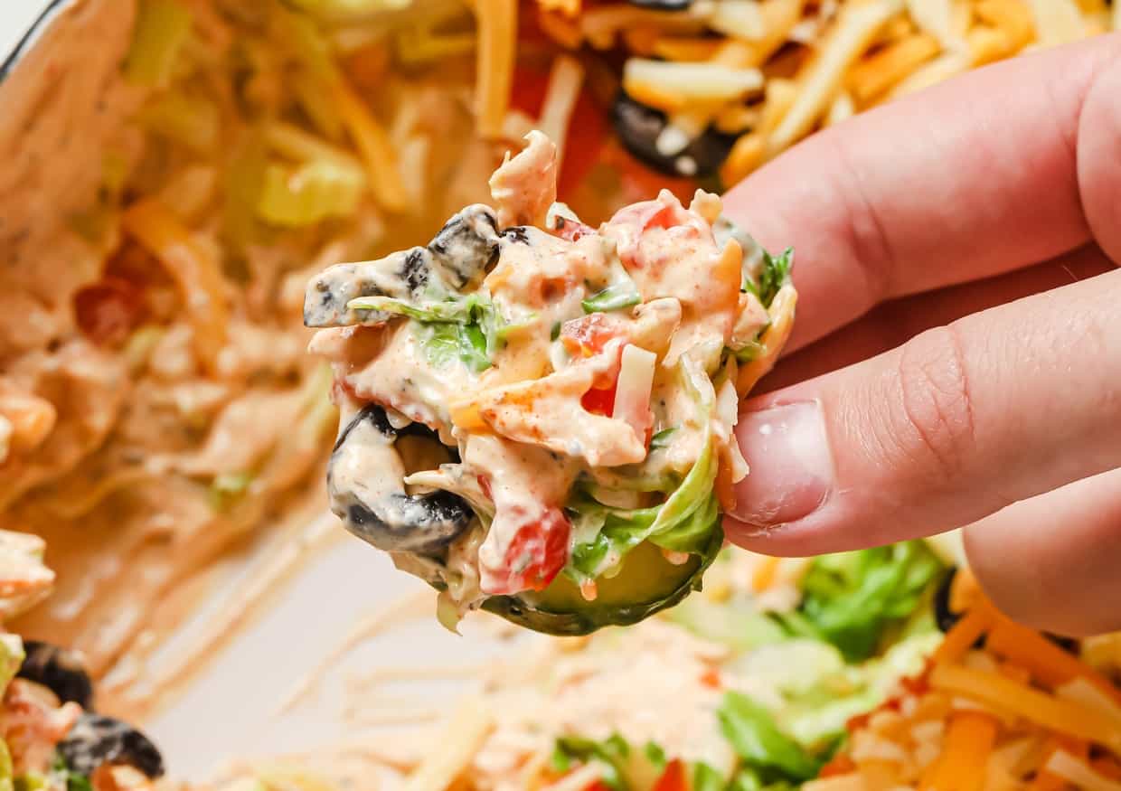 A hand holding a slice of cucumber topped with taco dip with cream cheese.