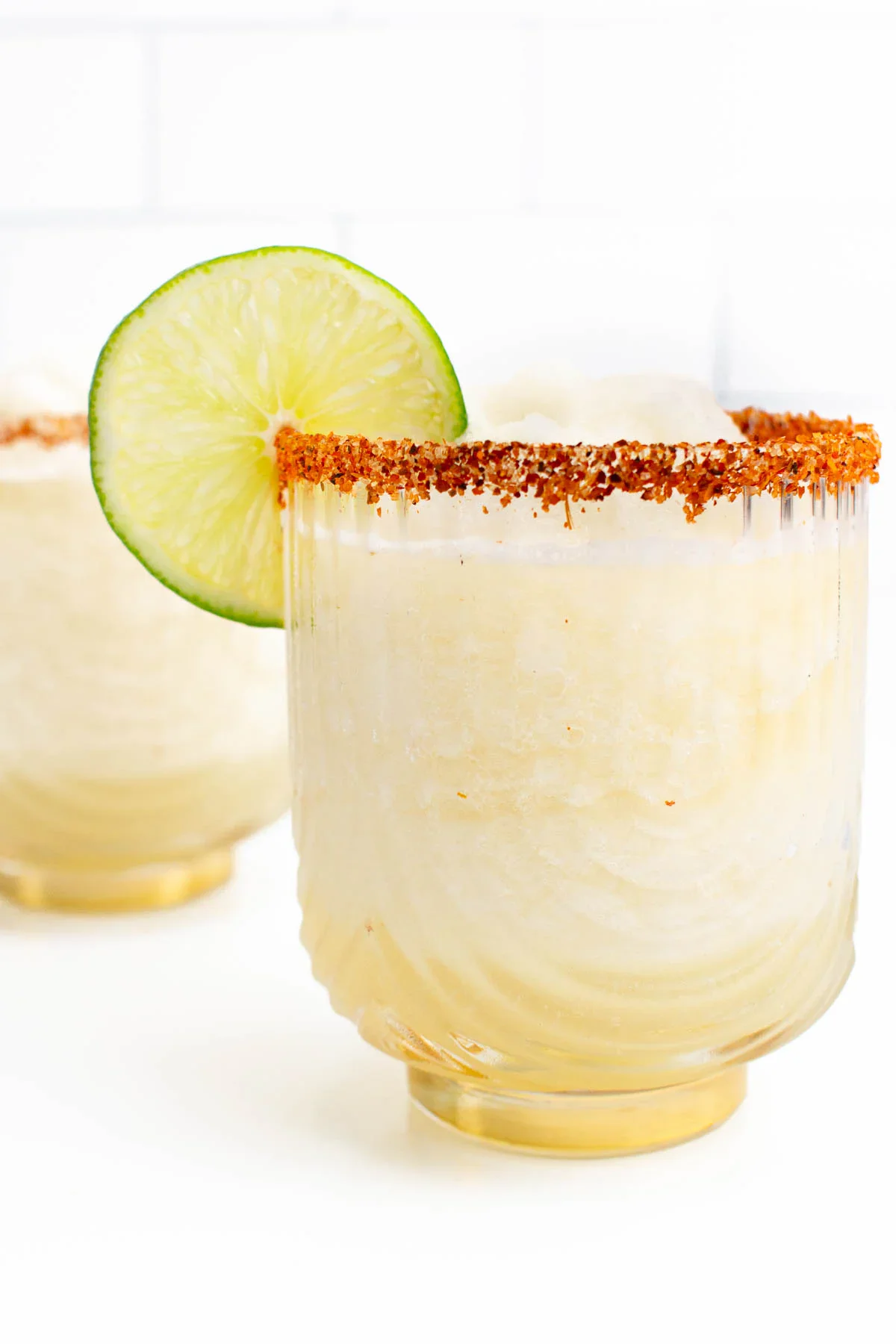 A glass of frozen margarita with a chili powder rim and a lime wheel garnish, set against a white background.