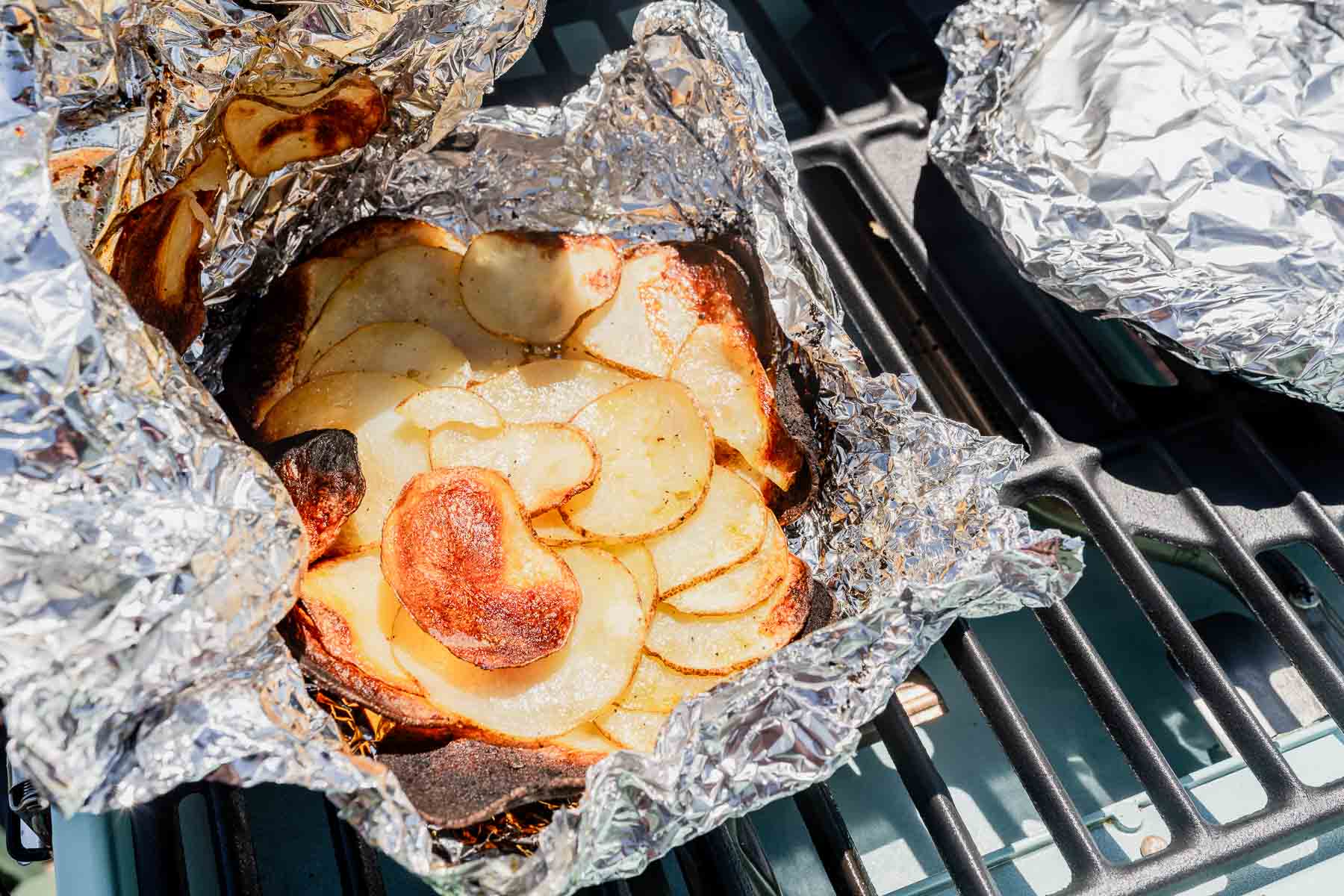 Grilled potatoes wrapped in foil resting on a grill plate.