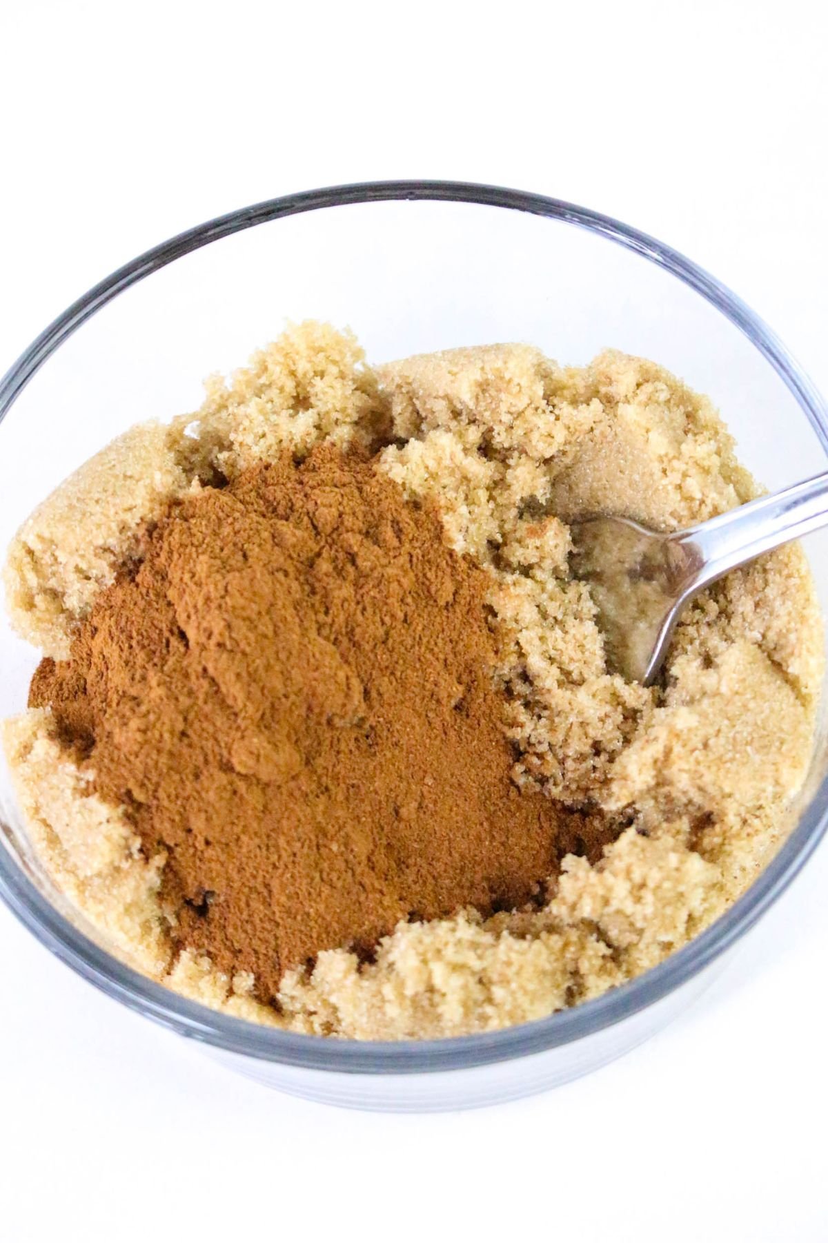 A glass bowl containing brown sugar and ground cinnamon with a spoon inside.