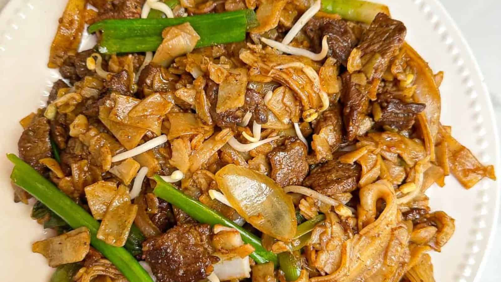 A plate of stir-fried noodles with beef, green beans, bean sprouts, and onions.