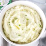 A bowl of mashed potatoes topped with two pats of butter and sprinkled with chopped parsley.