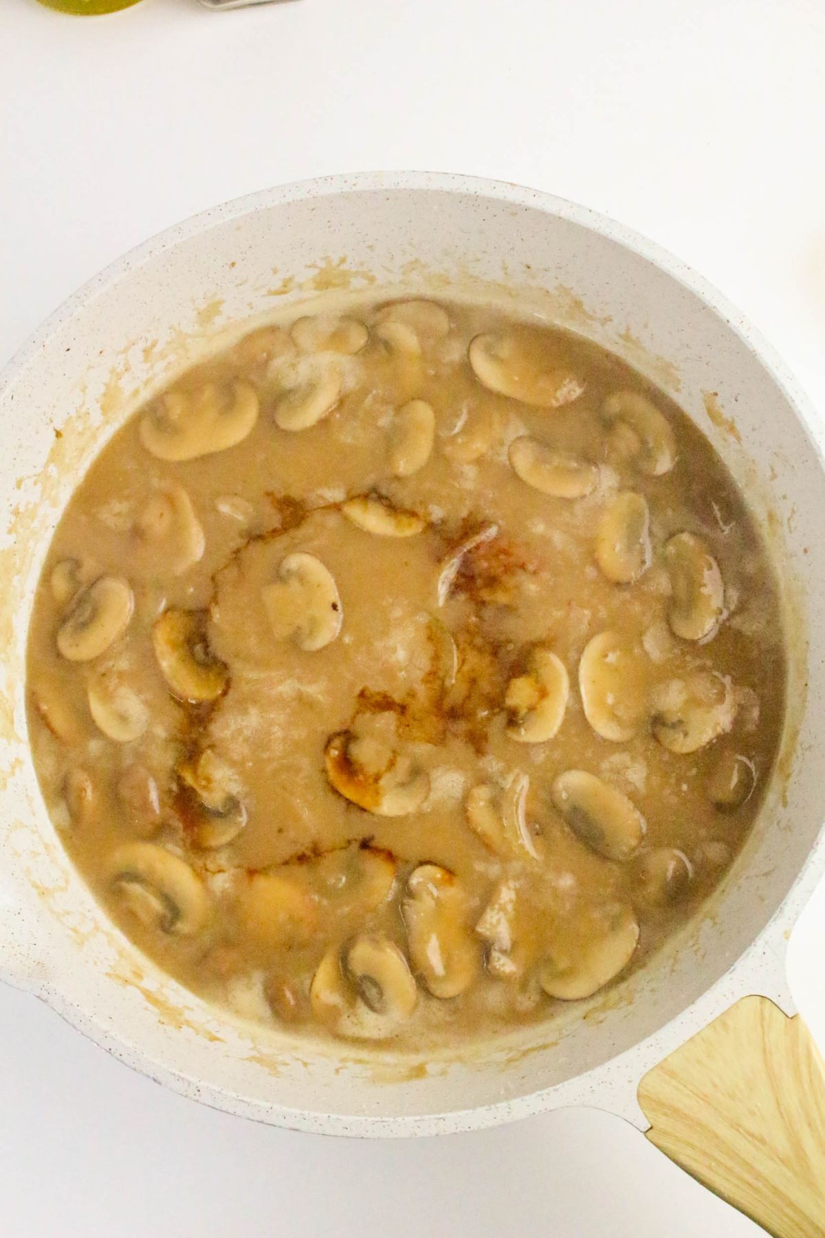 A white saucepan filled with mushroom gravy, showing sliced mushrooms in a thick brown sauce, on a white surface.