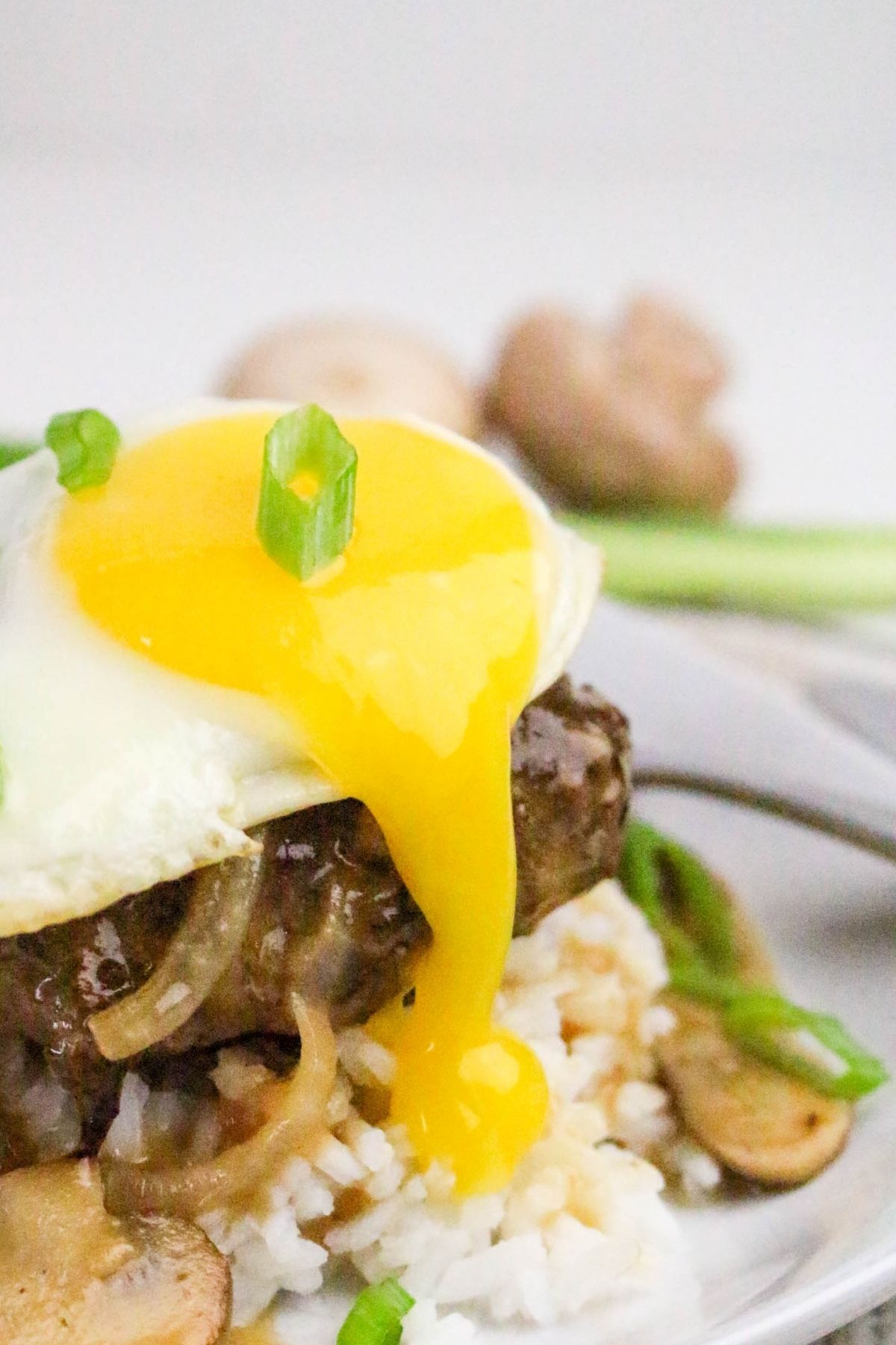 A hamburger steak topped with a sunny-side-up egg and green onions, served over rice with sliced mushrooms and onions, with egg yolk running down.