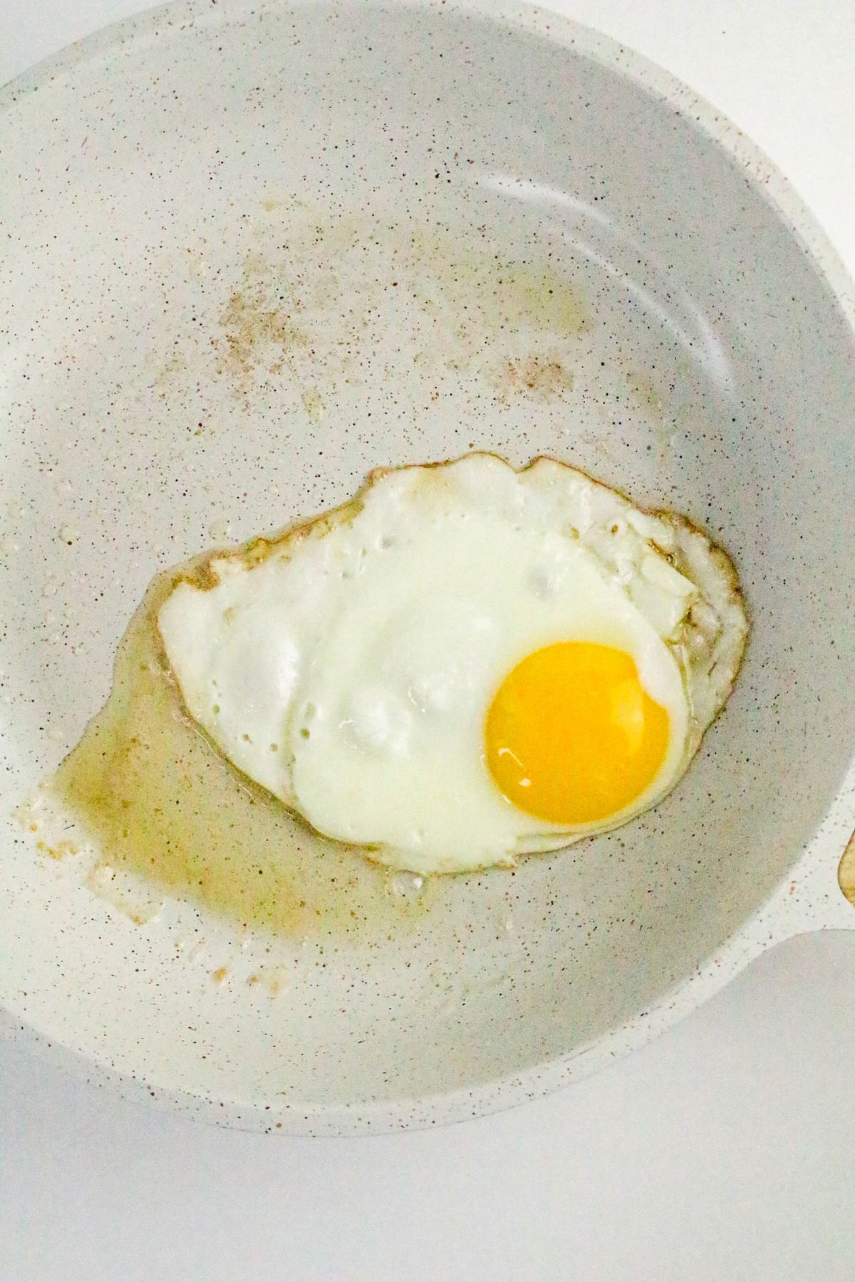 A single sunny-side up egg cooking in a white nonstick frying pan.