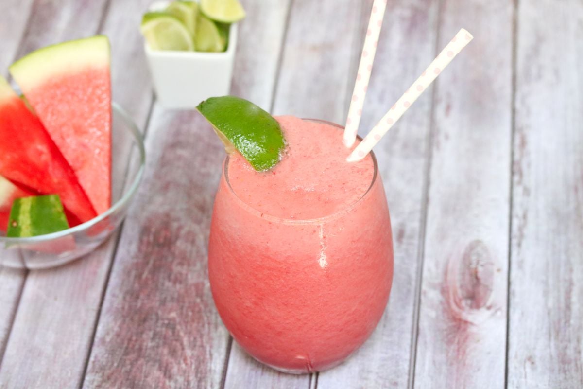 Pink watermelon slushie in a glass garnished with lime and more watermelon and lime behind it.