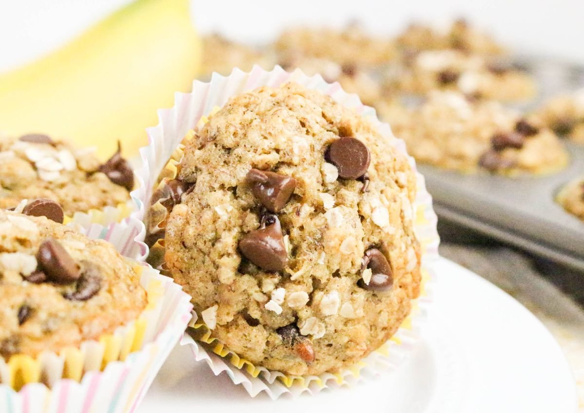 A close-up of an oatmeal banana muffin with chocolate chips, placed in a paper liner, with more muffins in the background.