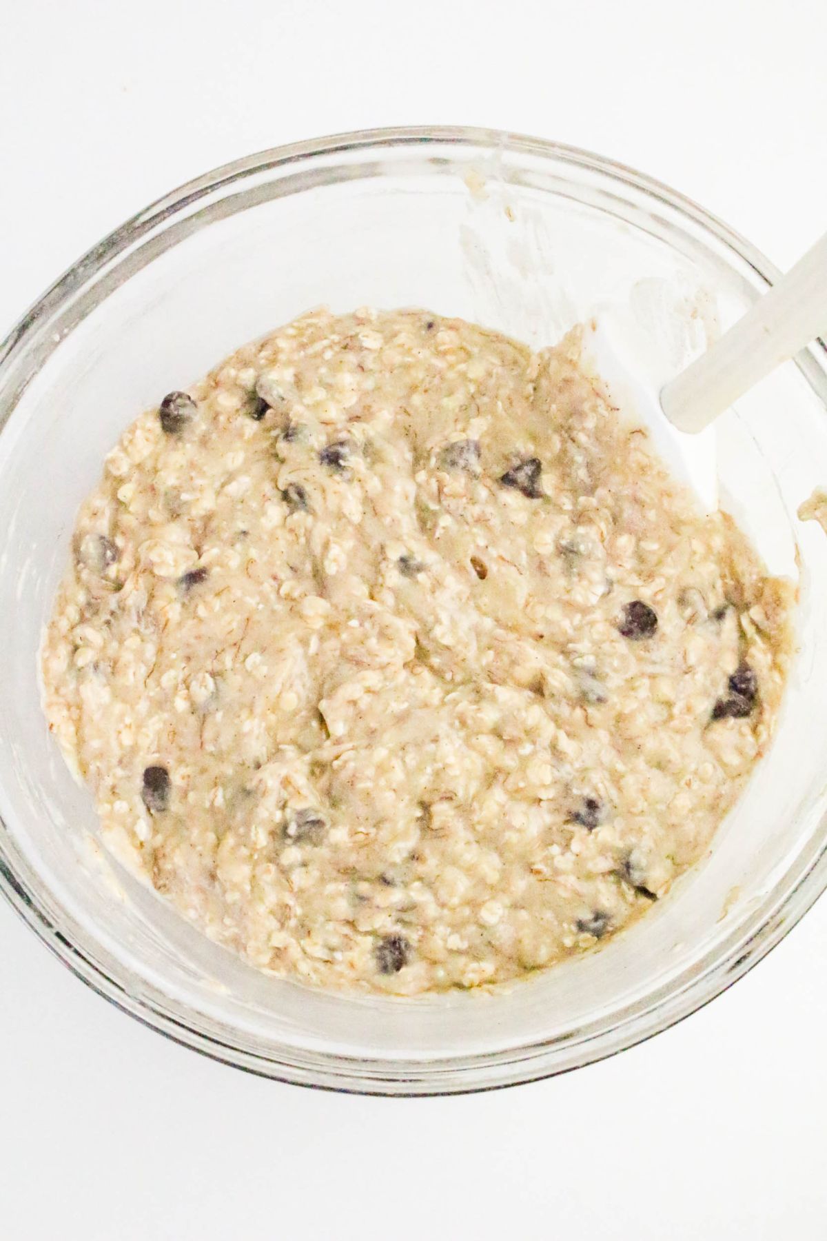 A glass bowl filled with oatmeal chocolate chip muffin batter and a spatula resting on the side.