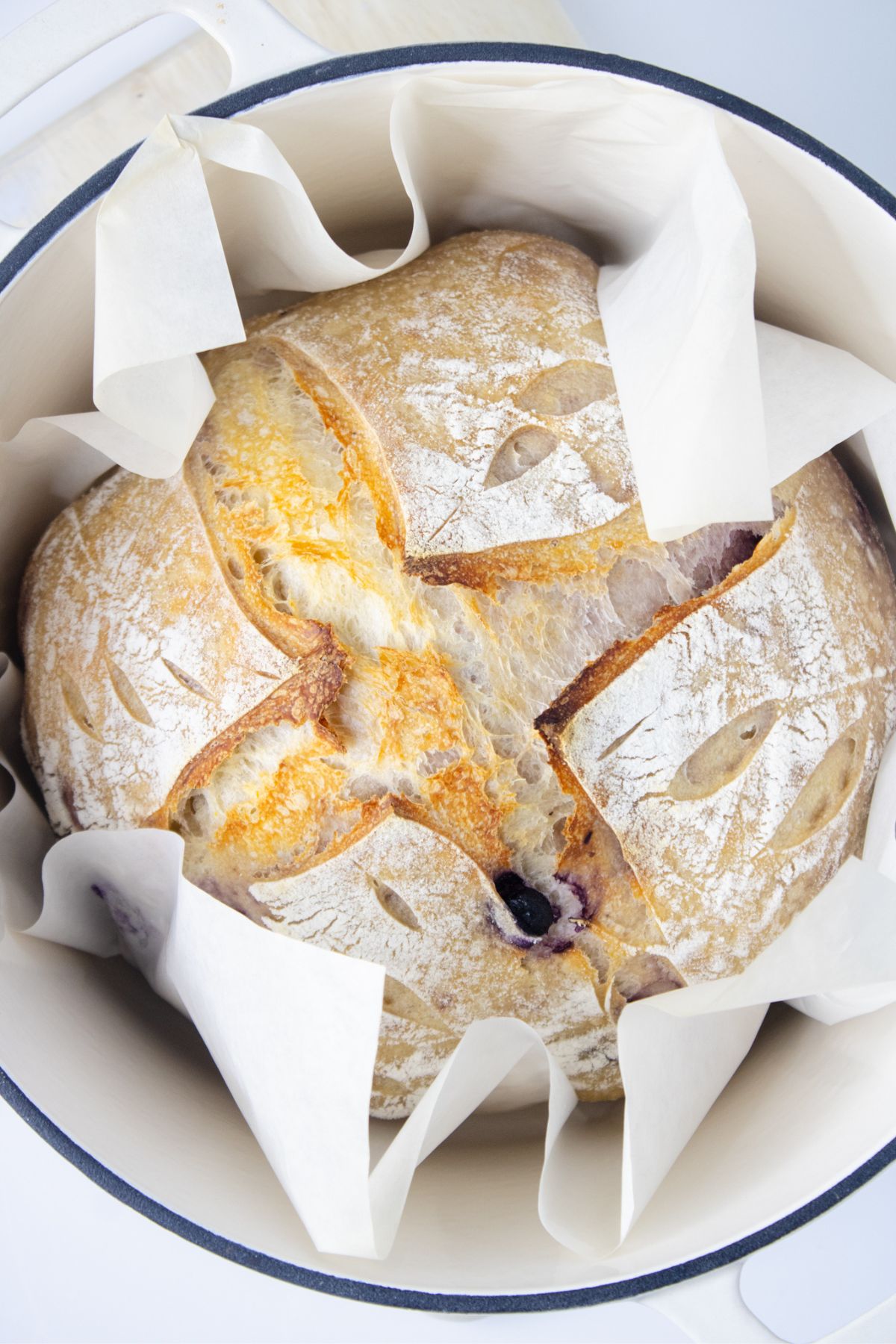 A round loaf of artisan sourdough bread with a scored crust, resting in a parchment-lined Dutch oven.