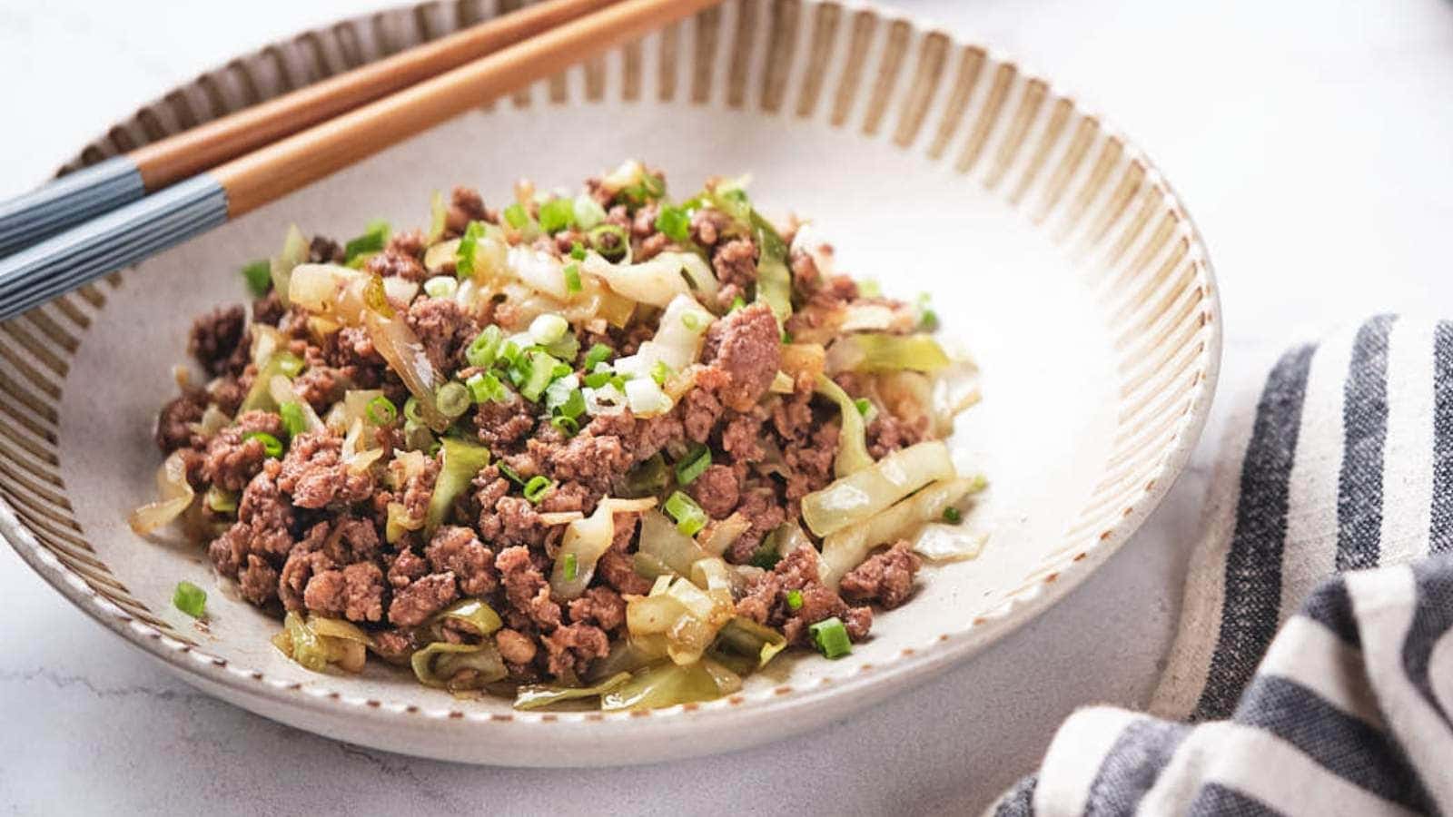 A plate of stir-fried ground beef with chopped cabbage and green onions, served with chopsticks on the side.