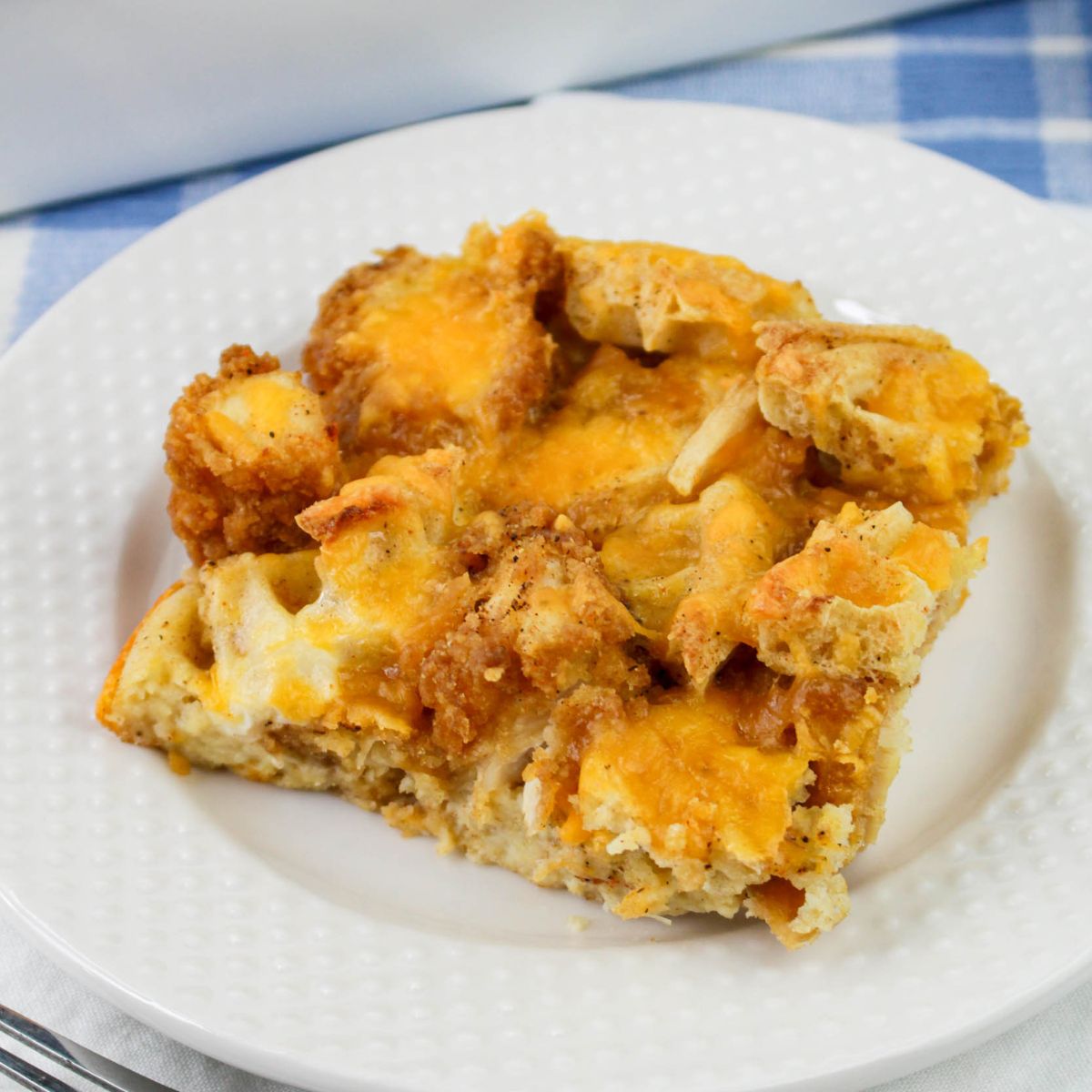 A serving of cheesy breakfast casserole with bread and melted cheese on a white plate.
