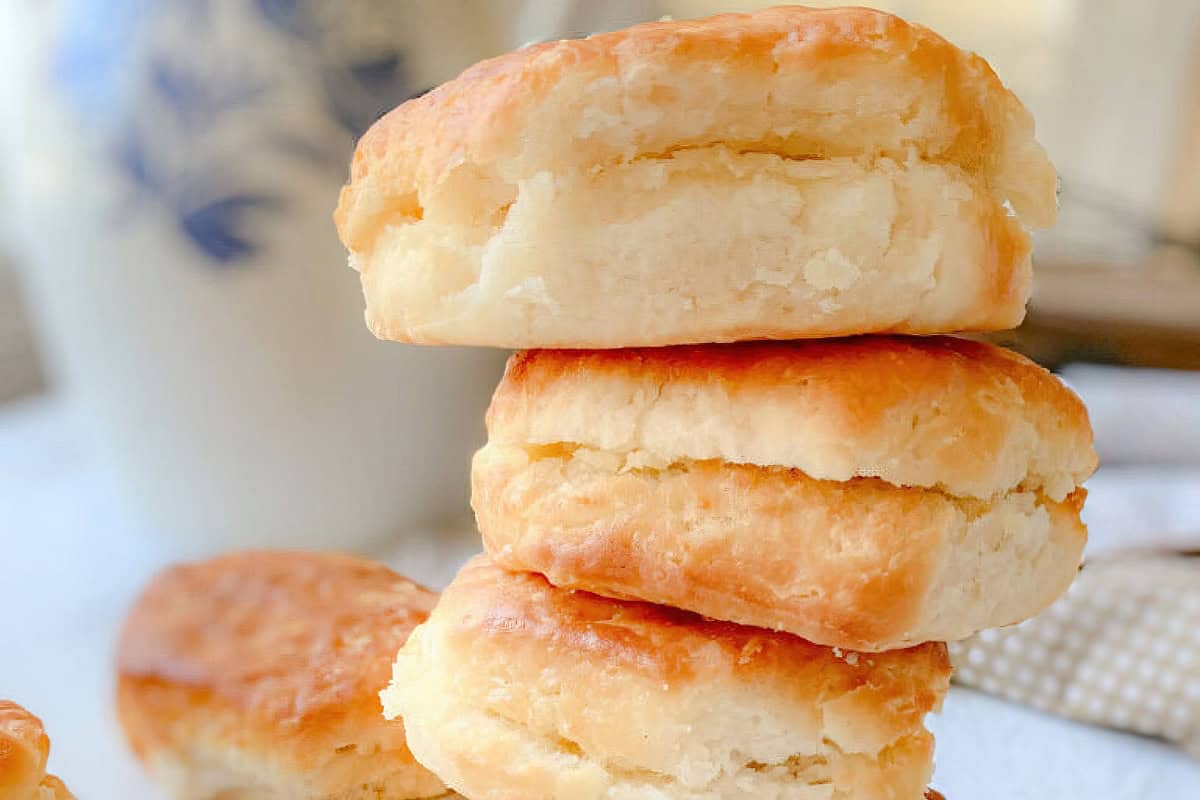 A stack of three golden-brown, flaky biscuits on a white surface, with a blurry background.