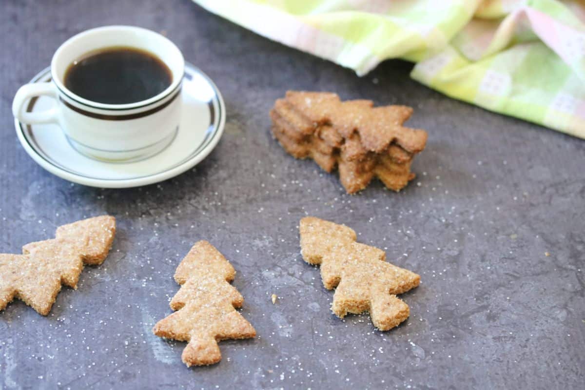 Almond flour sugar cookies in Christmas tree shape dusted with cane sugar around a cut of coffee.