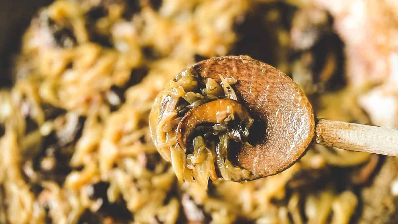 A closeup is shown of caramelized onions and mushrooms held on a wooden spoon.