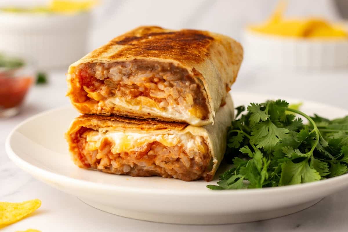 A close up image of cheesy bean and rice burrito on a plate.