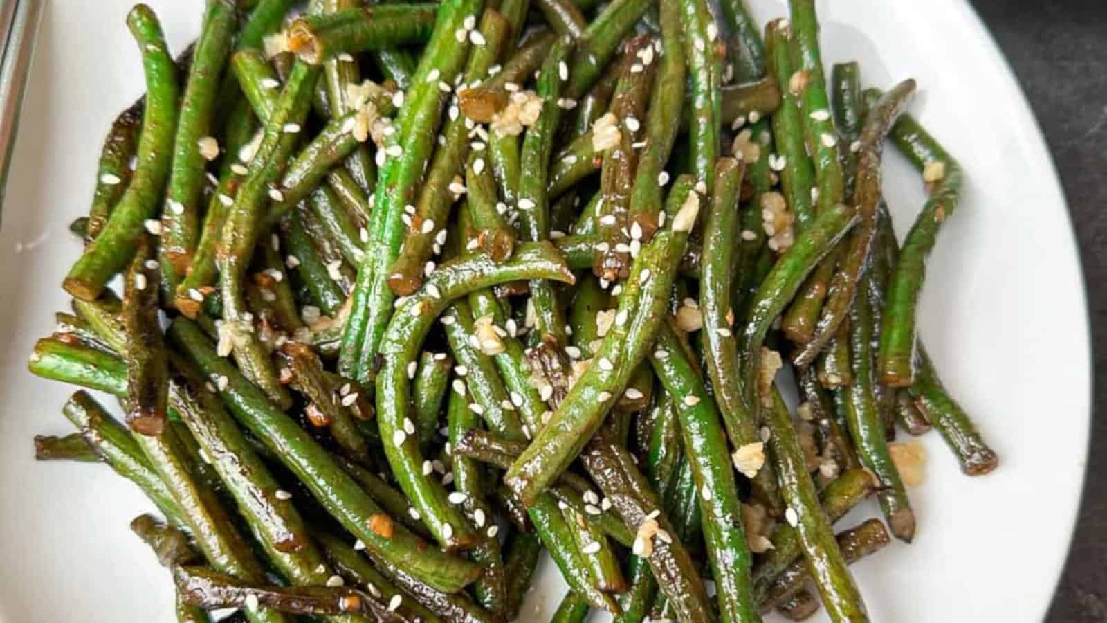 A plate of stir-fried green beans garnished with sesame seeds and minced garlic.
