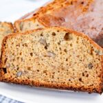 A close-up of a sliced loaf of banana bread with visible pieces of walnuts on a white plate.