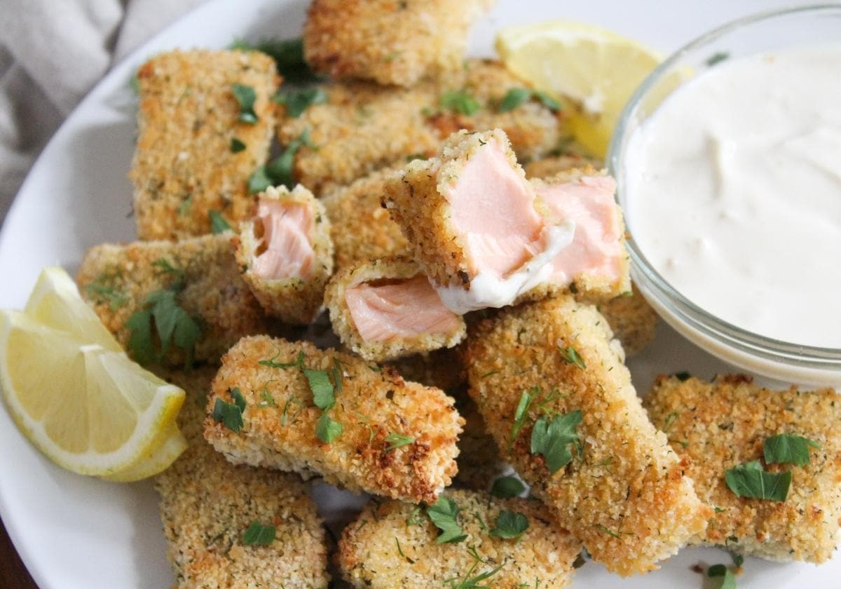 A pile of crispy salmon bites with a creamy white sauce in a small bowl beside it.