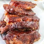A plate stacked with glazed, cooked barbecue pork ribs, featuring a shiny, caramelized sauce coating.