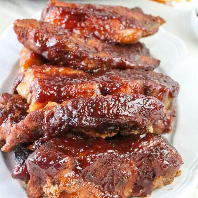 A plate stacked with glazed, cooked barbecue pork ribs, featuring a shiny, caramelized sauce coating.