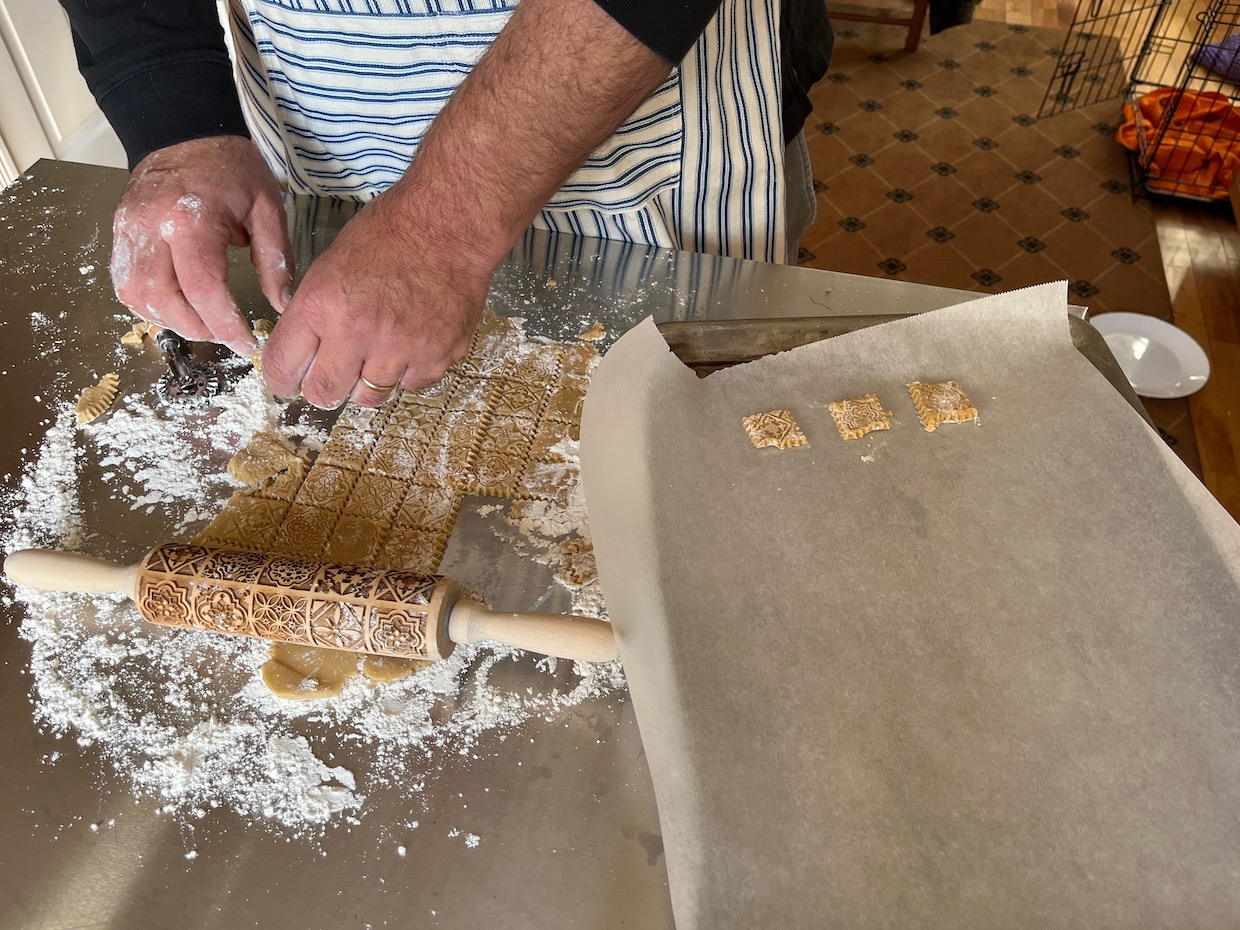A man is using an embossed rolling pin to roll out dough on a table.