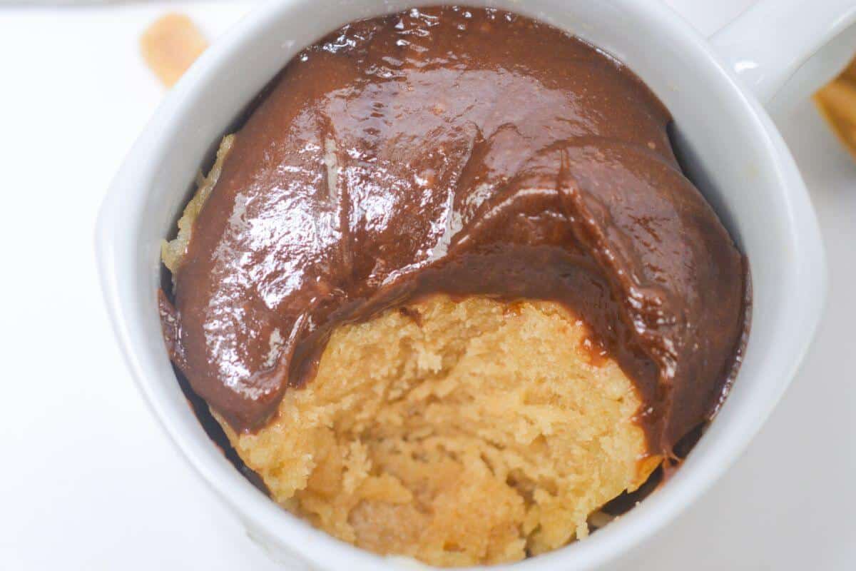 A partially eaten mug cake topped with chocolate frosting, shown in a white mug from a top-down view.