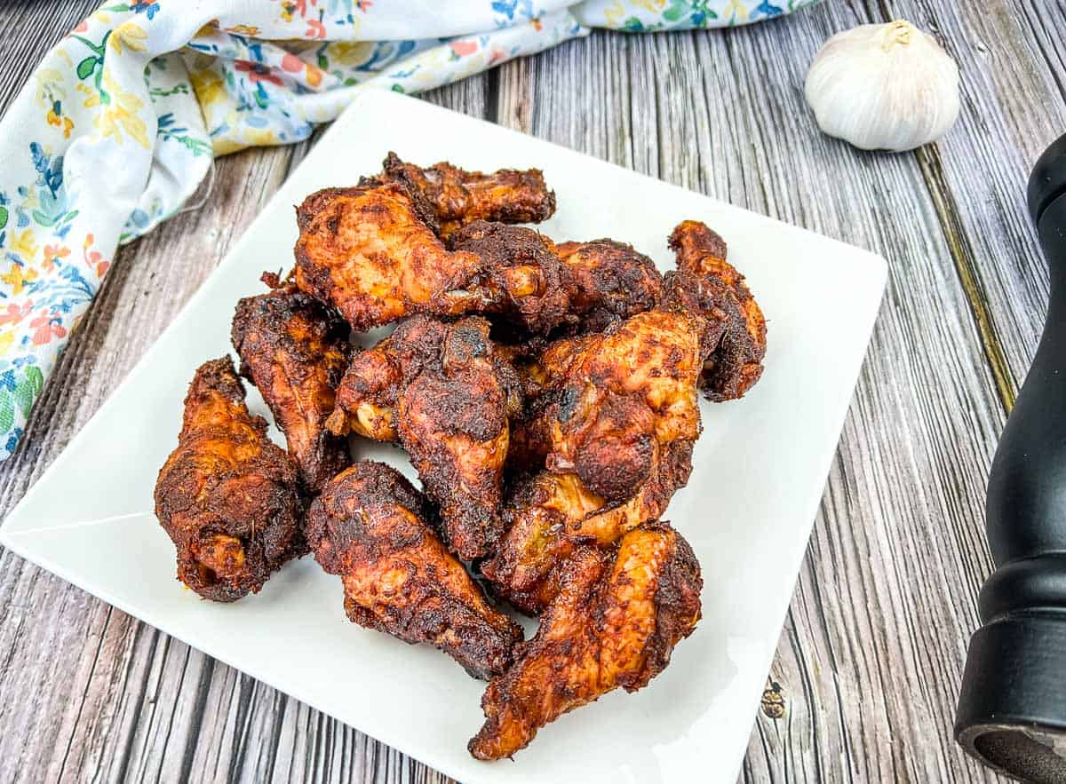 Smoked dry rubbed chicken wings on a white plate with garlic.