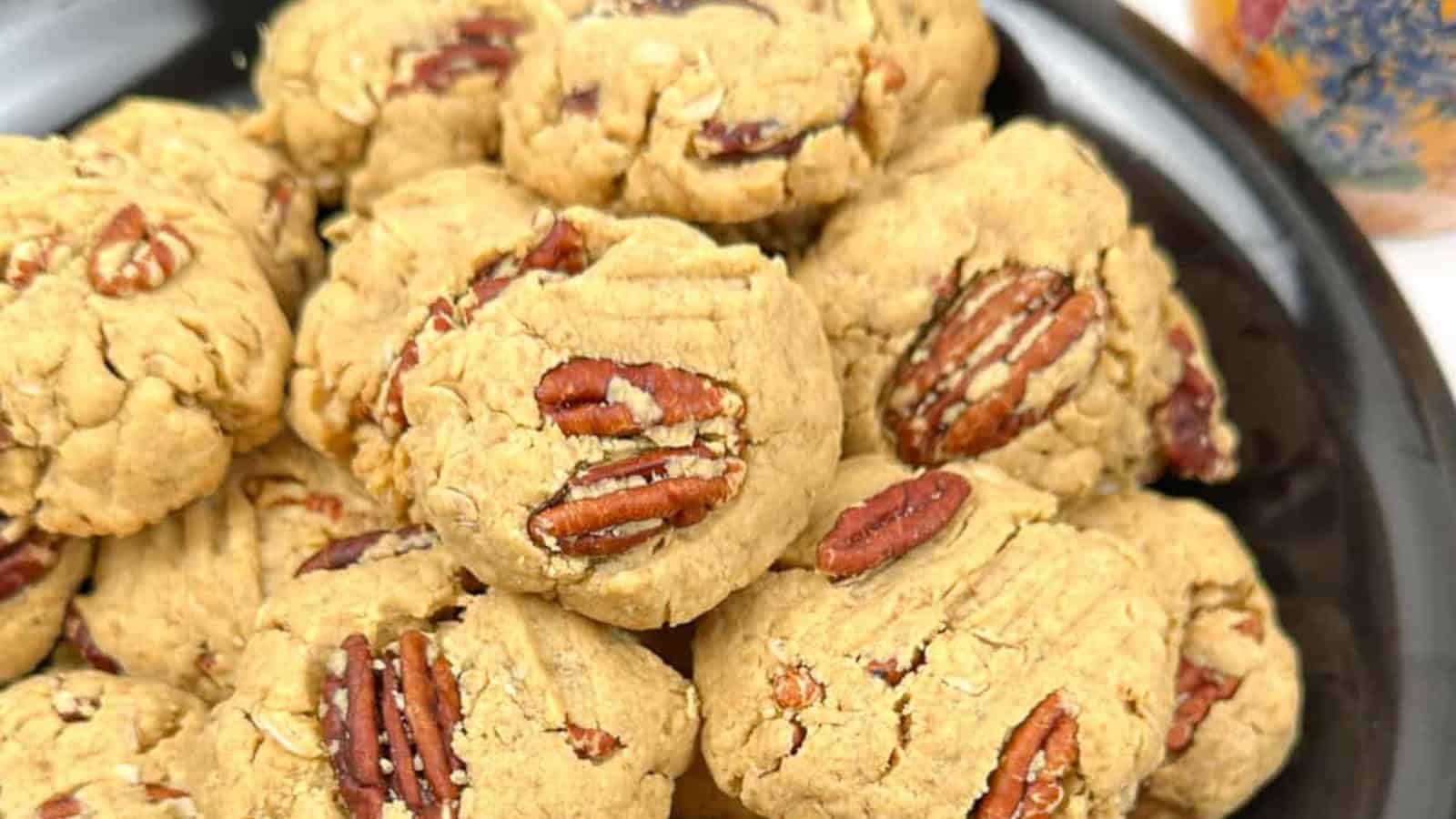 A plate of pecan cookies stacked together, showcasing a rough texture and visible pecan halves on top.