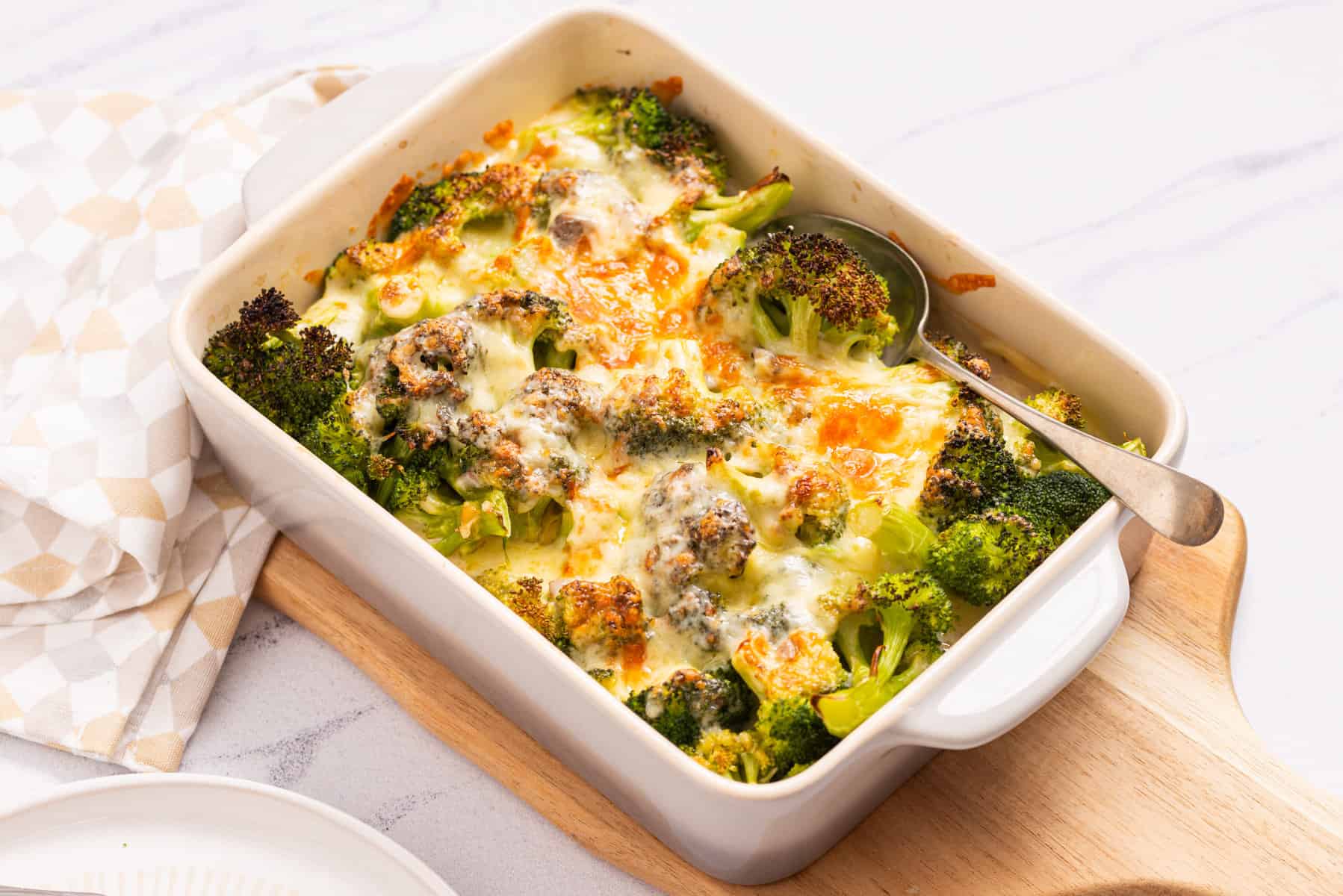 An image of broccoli cheese casserole served on a table with a spoon on the right side.