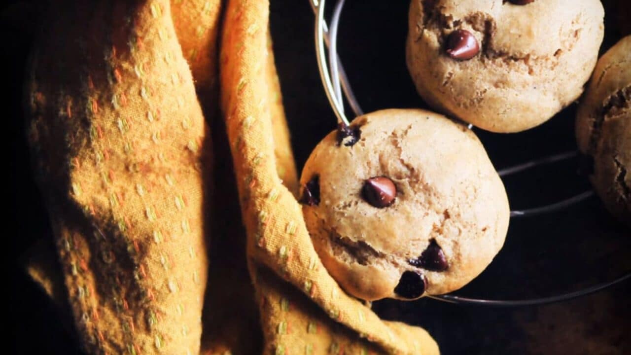 Chocolate chip cookies on a cooling rack next to an orange textured cloth.
