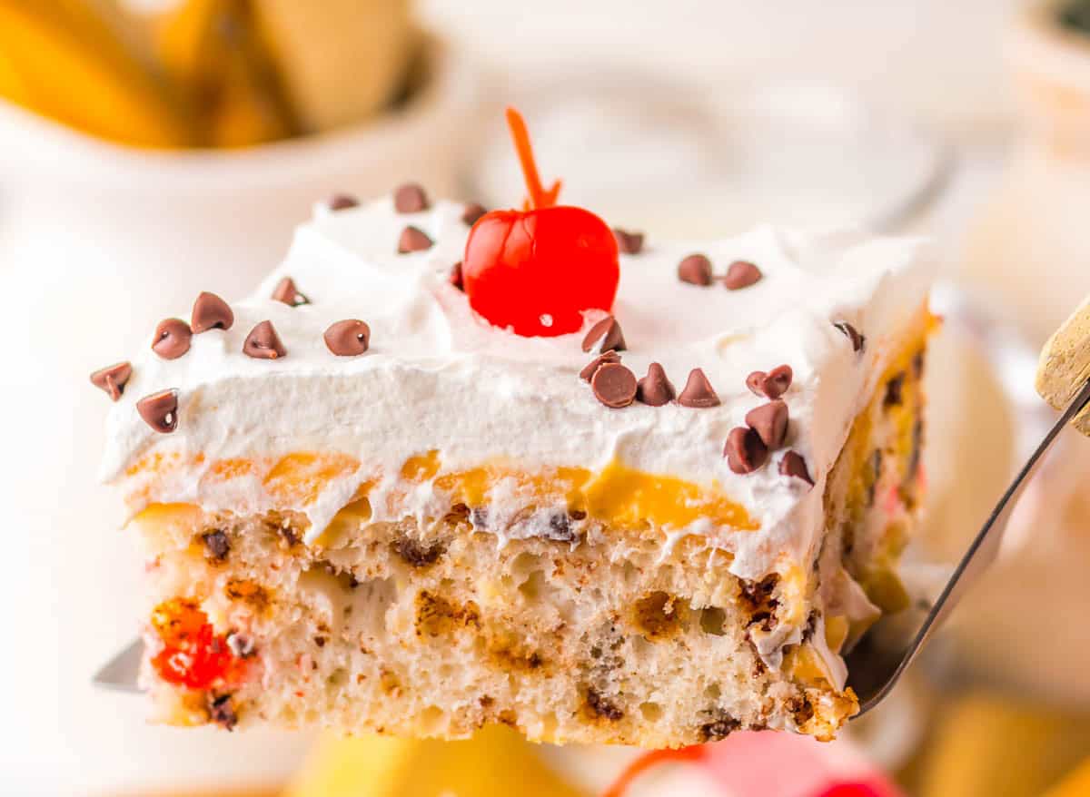A slice of cake with whipped topping, cherries and chocolate chip.