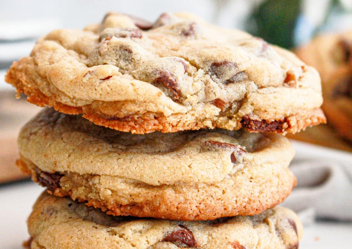 A close-up of three stacked chocolate chip cookies with a golden-brown, slightly crisp edge and soft center.