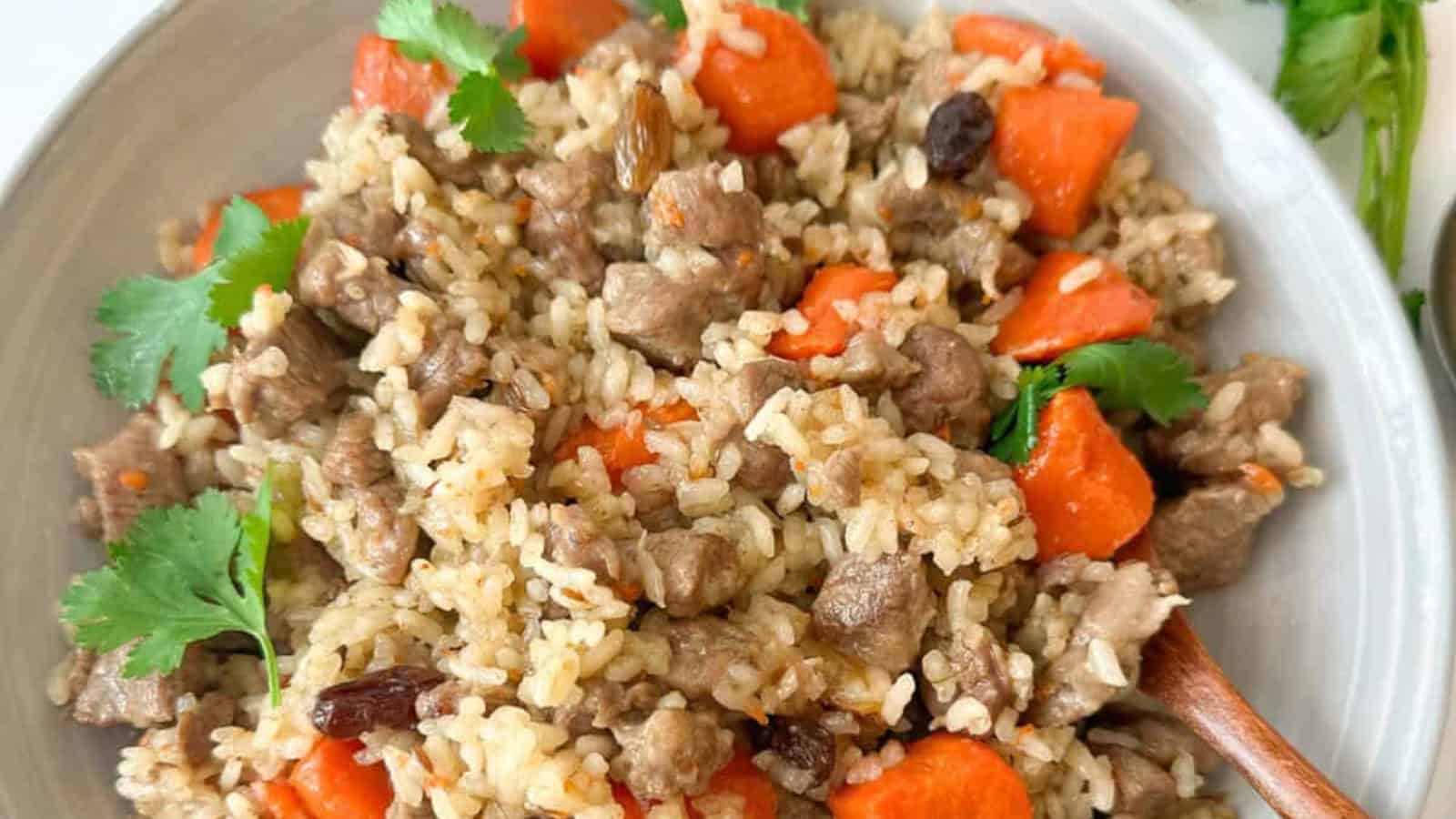 A bowl of rice pilaf with pieces of meat, carrots, raisins, and garnished with cilantro.
