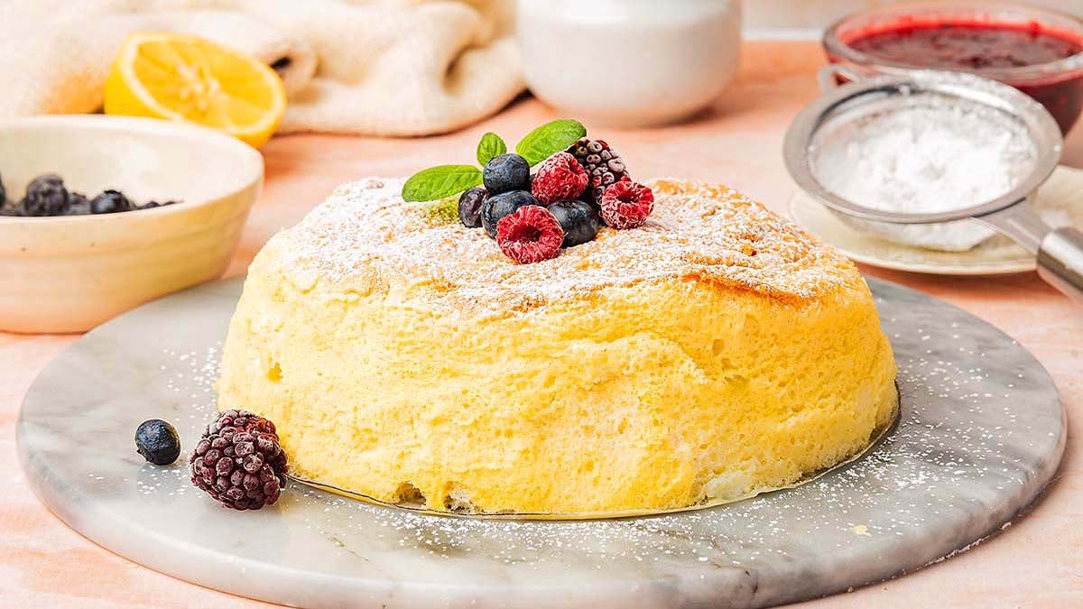 Fluffy Japanese pancake topped with raspberries, blueberries, and mint leaves on a marble platter.