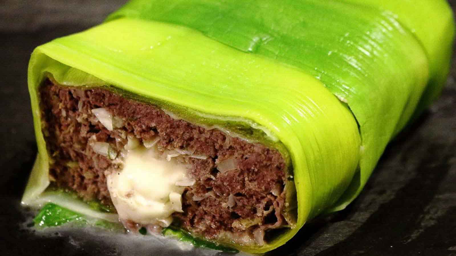 A slice of meatloaf wrapped in green vegetable leaves, with a melted cheese filling visible in the center.