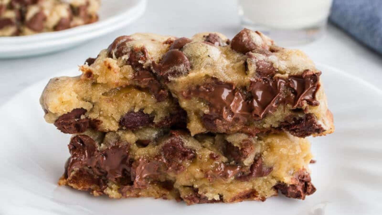 Two thick chocolate chip cookie bars stacked on a white plate, showing melted chocolate chips and a soft, gooey interior.