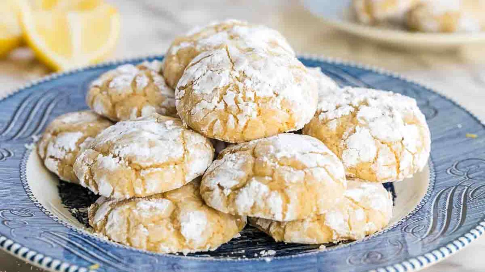 A plate of lemon crinkle cookies dusted with powdered sugar, stacked on a decorative blue and white dish.
