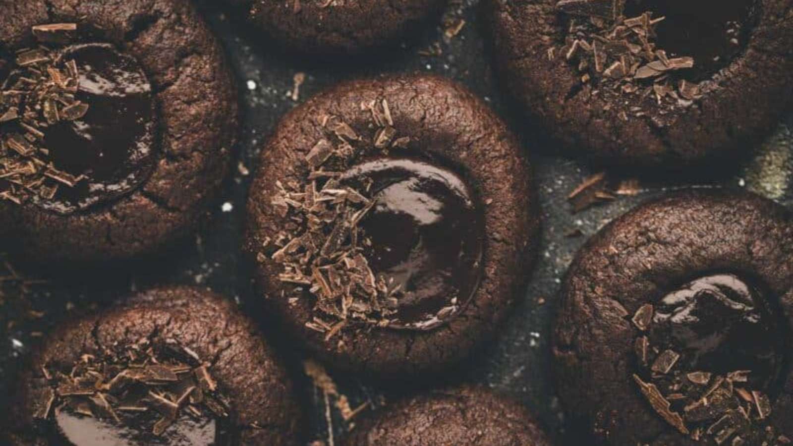 Close-up of several chocolate thumbprint cookies with glossy chocolate centers and chocolate shavings on top.