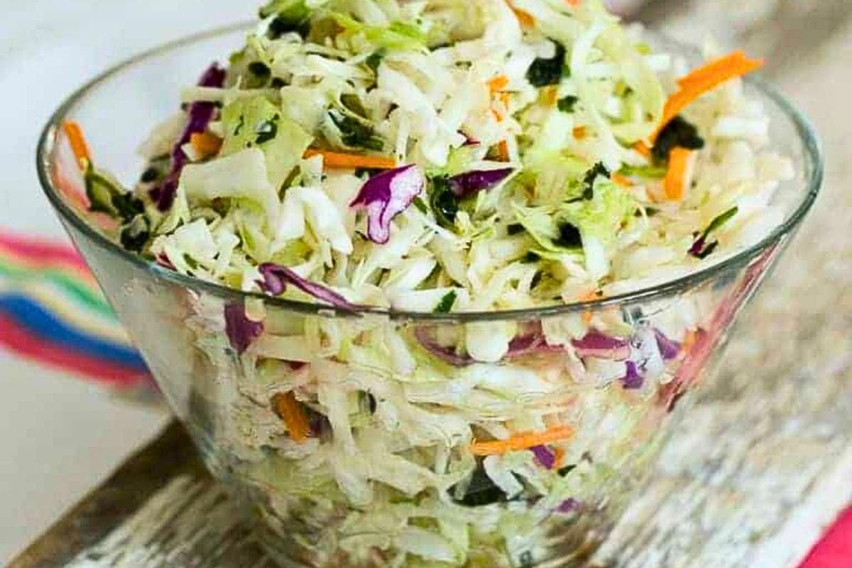 A glass bowl filled with shredded cabbage, carrots, and purple cabbage, resembling a fresh coleslaw salad.