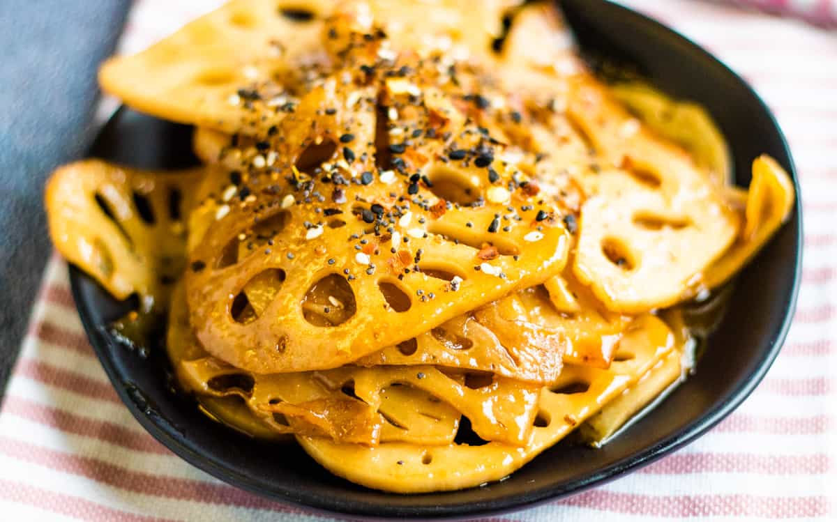 A low-angled shot of a pile of stir-fried lotus root on a black plate.