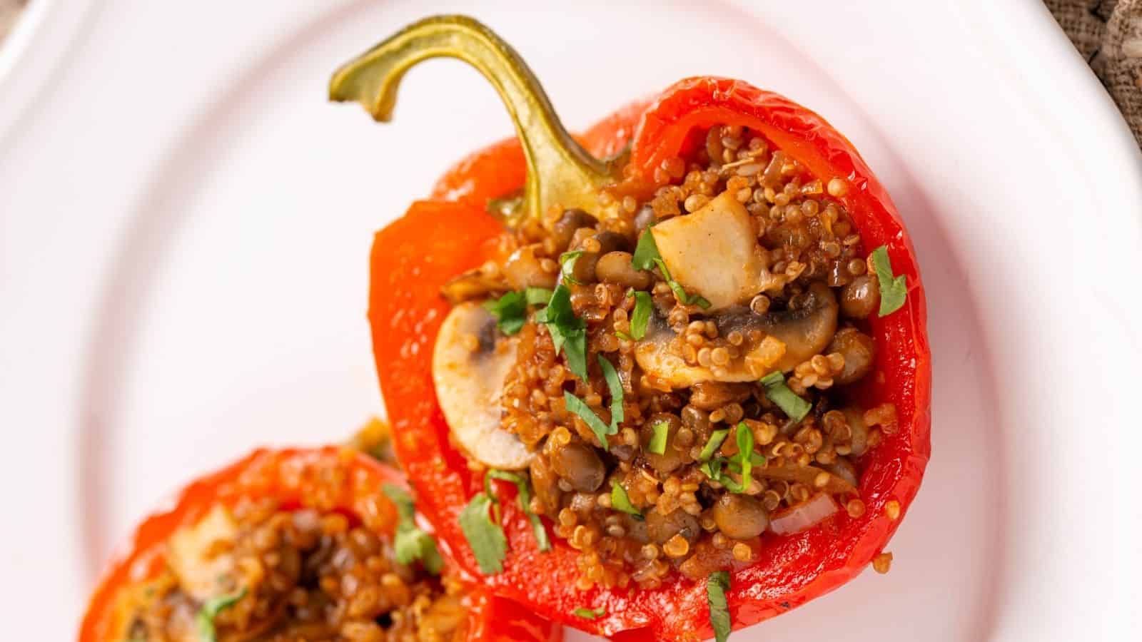 A photo showing vegan stuffed peppers arranged on a white plate, set atop a brown cloth, with a fork and knife placed beside.