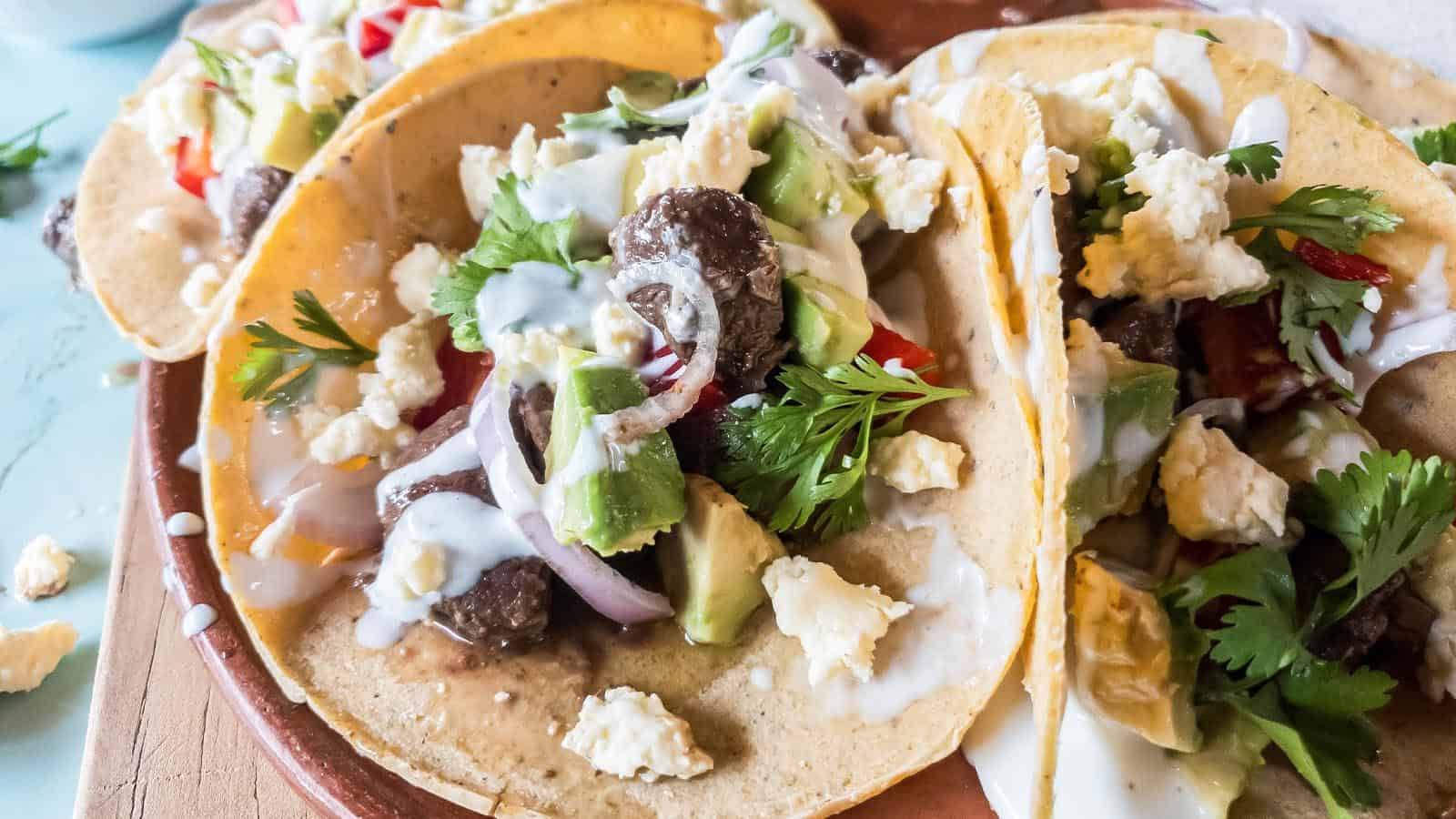 A picture of beef heart tacos with sour cream, avocado, red onion, and cilantro.