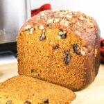 A sliced loaf of pumpkin bread with visible walnut pieces, placed on a wooden cutting board.